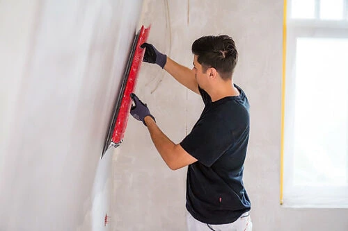 Handwerker glättet eine verputzte Innenwand mit einer langen roten Abziehlatte.