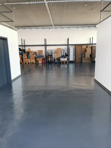 Lagerhalle mit grauer Bodenbeschichtung, weißen Wänden und Kartons auf Paletten im Hintergrund